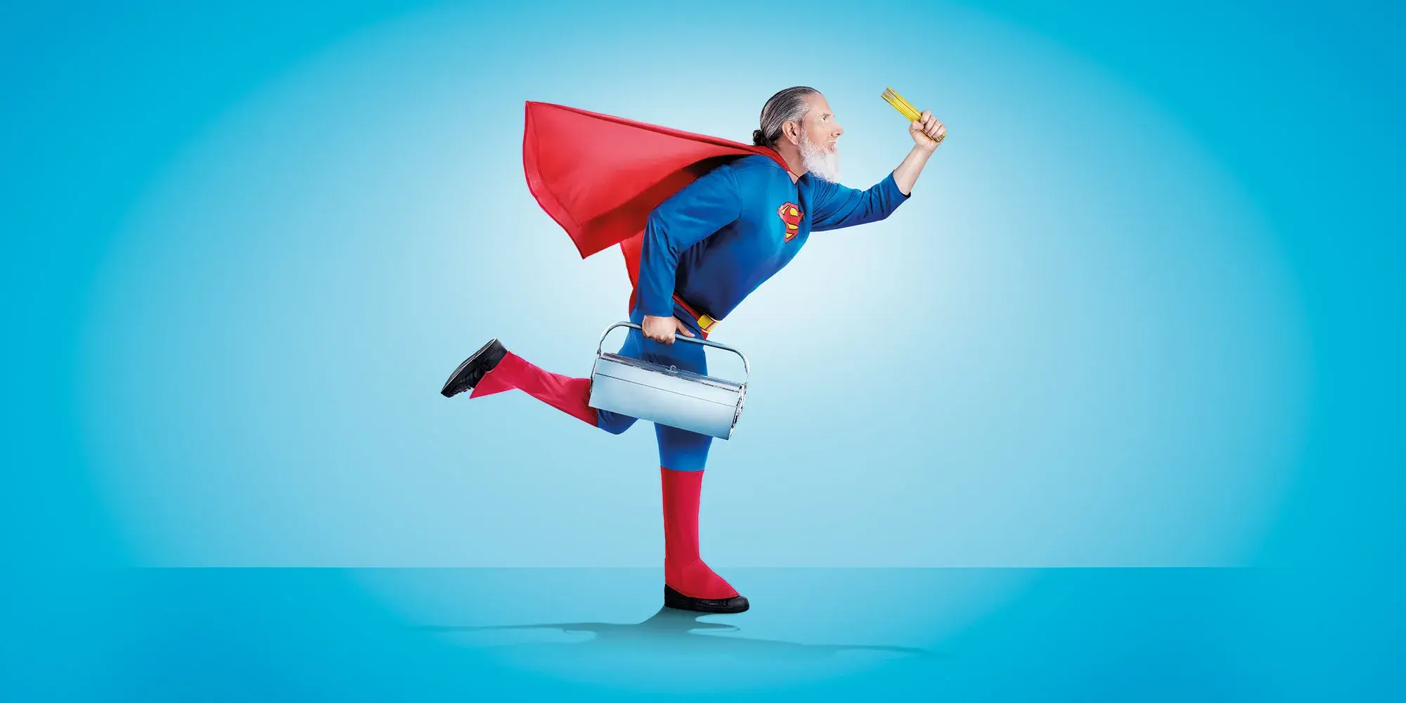 Bärtiger Mann im Superman-Kostüm mit Werkzeugkoffer im Laufschritt